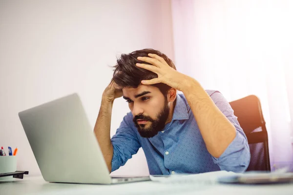Worried businessman using laptop in his office. Upset man holding his head.