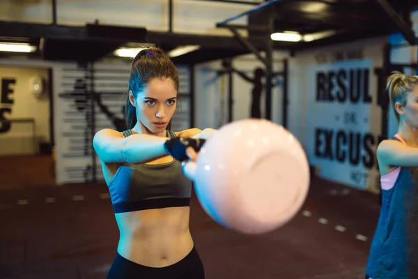 Fitness woman doing a weight training by lifting kettlebell. Muscular fitness woman, holds up a pink kettlebell crossfit the gym. Fitness woman in the gym. Crossfit woman. Crossfit and fitness