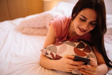 Yatakta yatıyordu ve smartphone kullanarak güzel kız.