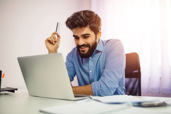 Alışveriş online kredi kartı ve dizüstü bilgisayar ile gülümseyen bir adam portresi. Evden alışveriş online.