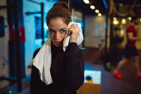 Tired girl wiping sweat with towel in gym.