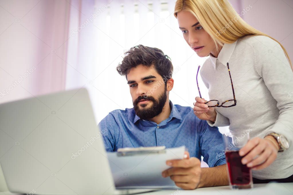 Young businessman and woman working together in office with laptop and mobile