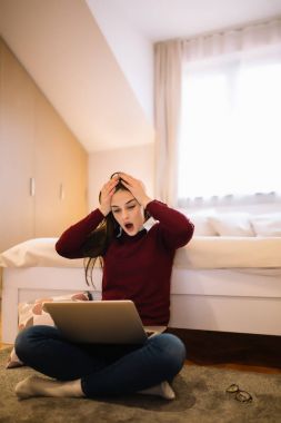 sinir kız yatak odasında yere otururken dizüstü bilgisayarda internet üzerinde sörf. Dikey vurdu.