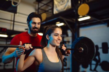 Genç kadının kişisel bir eğitmen ile spor salonunda bodur egzersiz yapması.