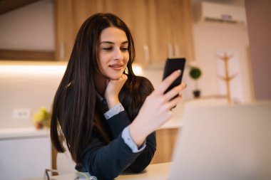 Evdeki bir masada birden fazla cihaz kullanarak çalışan mutlu kadın.