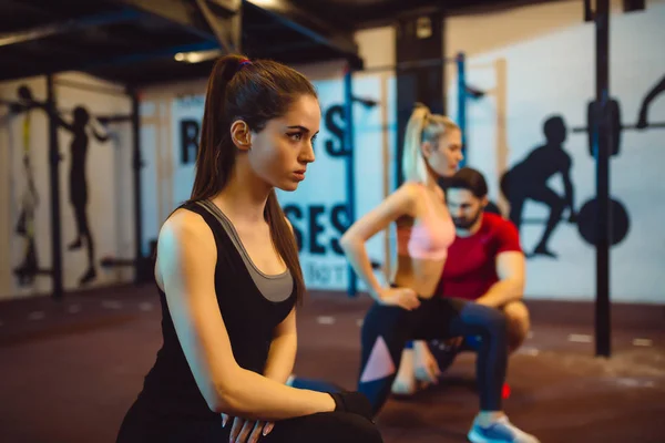 Two sporty women doing exercises with assistance of their personal trainer in gym. — Stock Photo, Image