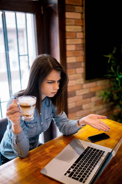 年轻不愉快的混乱的商业妇女坐在室内在咖啡馆使用膝上型电脑 紧张的女孩问题在线或电子邮件通知 — 图库照片
