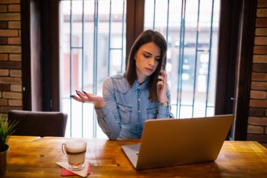 dizüstü bilgisayar kullanarak ve telefonda konuşurken bir işkadını