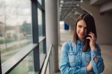 Genç casual giyimli kadın yüzünde gülümseme ile telefon görüşmesi geçiriyor