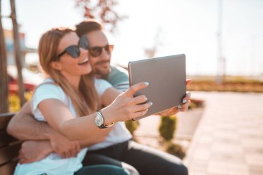 Onlar bankta oturmuş selfie alarak güneş gözlüğü ile güzel genç Çift