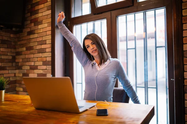 Young girl stretches after she finished with work on hers laptop in cafe