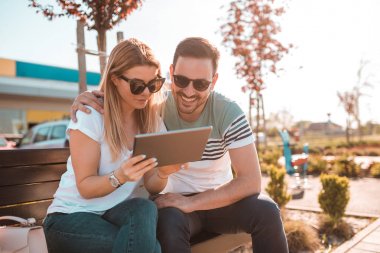 Süre dışında bir bankta oturan ve onların tablete Internet tarama genç adam kız arkadaşının omzuna elini tutuyor