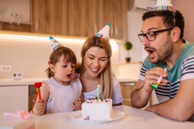 Mutfakta oturuyor iken sevimli küçük kız mum bir doğum günü pastası ailesiyle birlikte darbeler