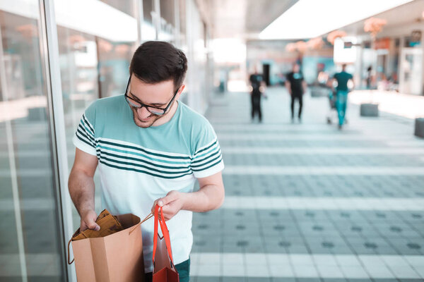 Young man with glasses is checking his shopping bags to be sure that he bought everything that he needs