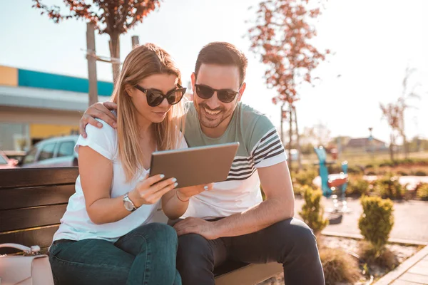 Süre dışında bir bankta oturan ve onların tablete Internet tarama genç adam kız arkadaşının omzuna elini tutuyor