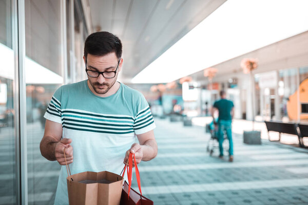 Young man with glasses is checking in shopping bags whether he bought everything from the list