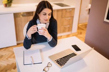Kahve içme sırasında dizüstü bilgisayar önünde oturma genç iş kadını