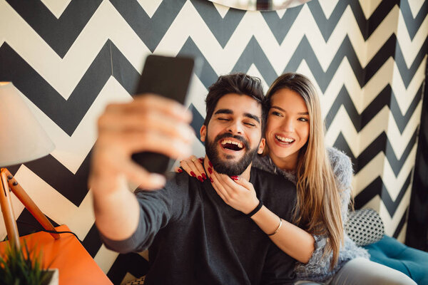 Young man with beard taking selfie with girlfriend while sitting in cafe