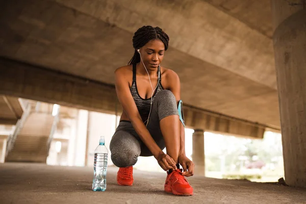 Young african american woman tying up sneakers before start running