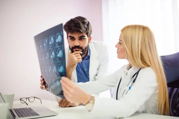 Young Blonde Female Doctor Analyzing Ray While Her Colleague Sitting — Stock Photo, Image