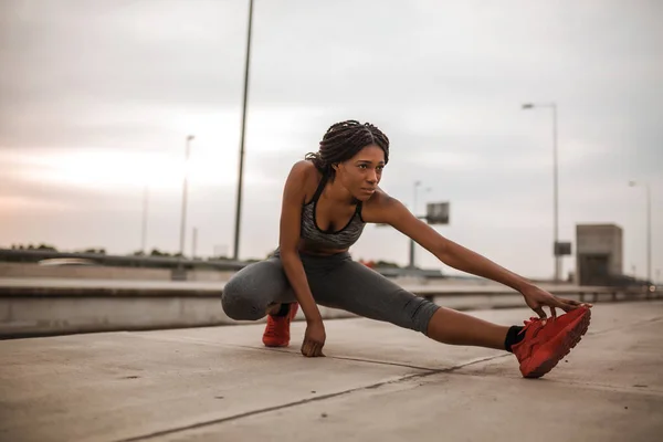 Young african american woman doing warming up and stretching her leg before morning run