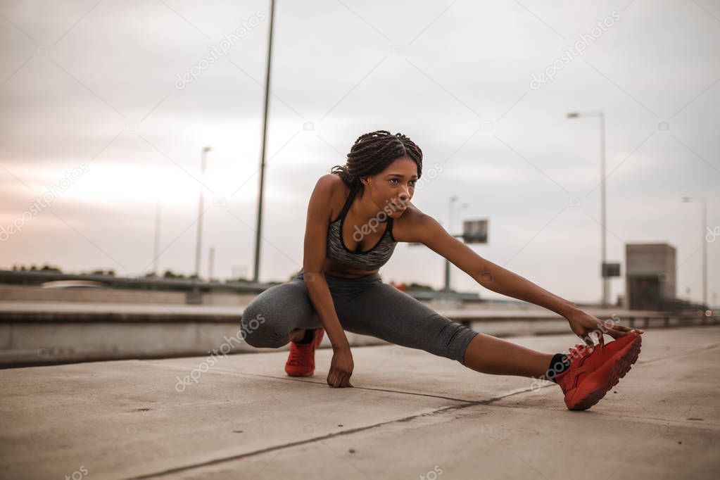 Young african american woman doing warming up and stretching her leg before morning run