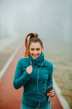 Atkuyruklu genç bir kadın sisli ve soğuk bir günde parkta koşuyor. Sisli bir günde dışarıda koşan kızın yakın fotoğrafı..