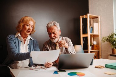 Yaşlı sarışın kadın ve gri saçlı adamın ofis masasında otururken grafiklere baktığı yakın bir fotoğraf..
