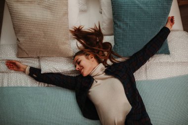 Yatağında uzanan balıkçı yaka kazak ve ekose gömlek giyen güzel esmer kız manzarası..