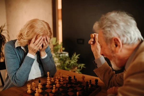 Portrait of blonde woman with face in hand because she made wrong move in chess game against her husband.