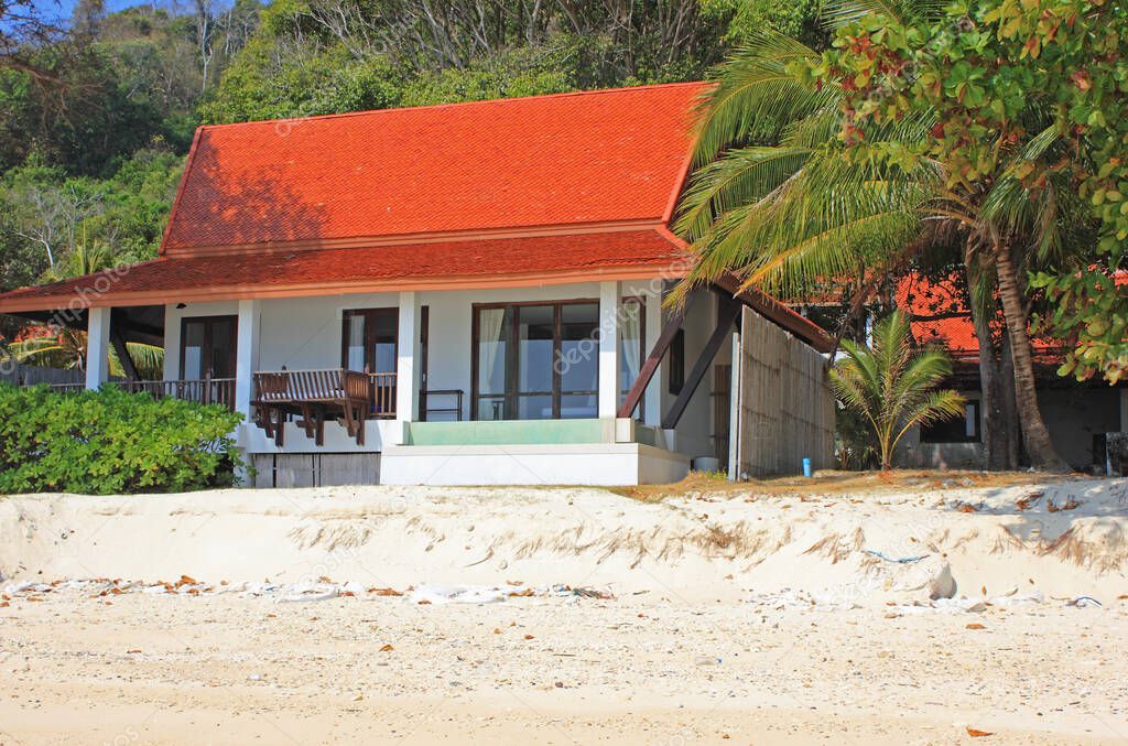Maiton island, Thailand - February 2, 2020: Villa with white walls, black window frames and red tile roof on the beach. Sand beach in foreground and rainforest in background. Maiton private island offers villas for overnight stay.