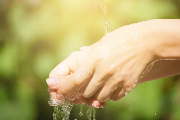 Woman washing hand outdoors. Natural drinking water in the palm. Young hands with water splash, selective focus. Instagram yellow toned — Stock Photo, Image