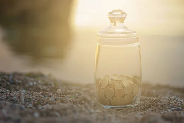 Investment, passive income and saving concept. Coins in a glass jar on the beach in rays of the sun