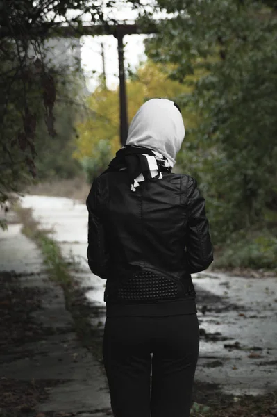 Вертикальний вид ззаду сумної жінки з шарфом на голові біля порожньої лісової дороги. Концепція очікування і смутку — стокове фото