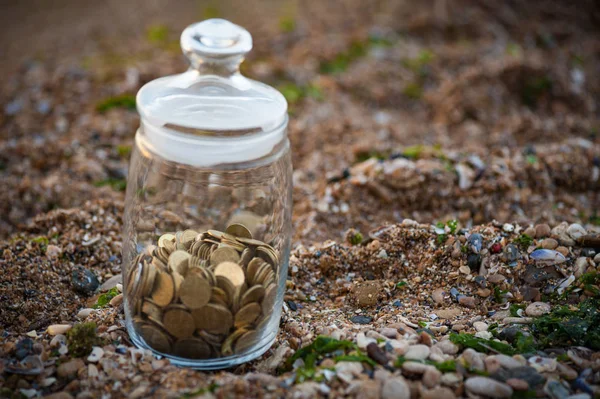 Investment, passive income and saving concept. Coins in a glass jar on the beach in rays of the sun