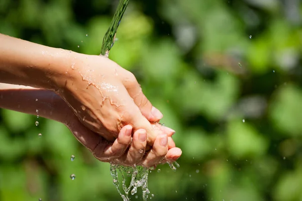 Женщина моет руки на улице. Естественная питьевая вода в ладони. Молодые руки с брызгами воды, избирательный фокус — стоковое фото