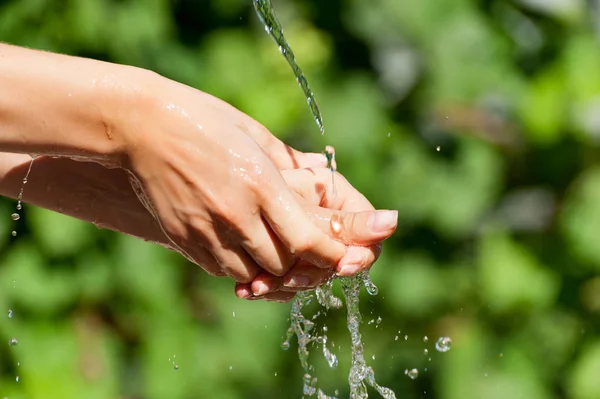 Женщина моет руки на улице. Естественная питьевая вода в ладони. Молодые руки с брызгами воды, избирательный фокус — стоковое фото