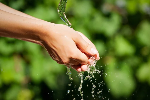 Woman washing hand outdoors. Natural drinking water in the palm. Young hands with water splash, selective focus