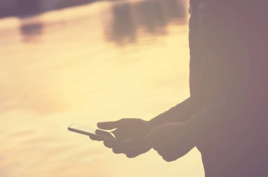 Kadın suyun kenarında duran, akıllı telefon kullanarak ve bekleyen biri, yan görünüm, Instagram etkisi veya filtre