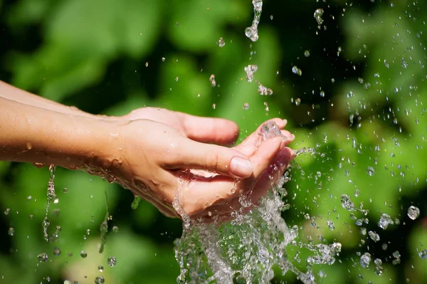 Donna che lava le mani all'aperto. Acqua potabile naturale nel palmo della mano. Mani giovani con spruzzi d'acqua, focus selettivo — Foto Stock