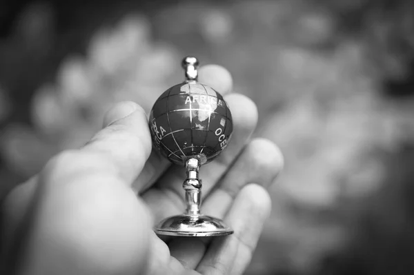 Man hand is holding small globe outdoor. Concept of travelling and adventure, blur background. Black and white filter or effect