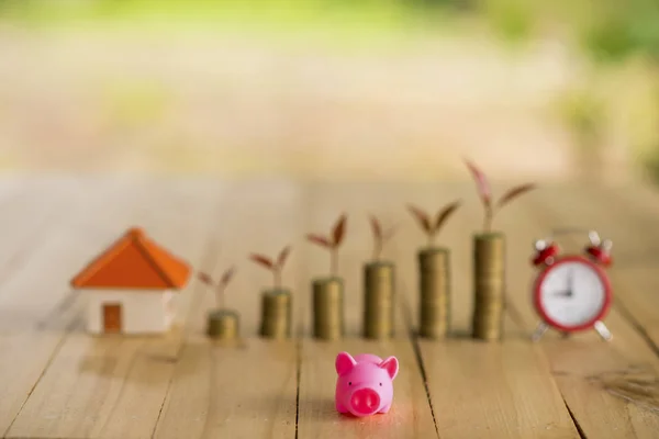 Ein Sparschwein auf dem stapelbaren Goldmünzen und Tafel Haus und Uhr auf dem alten blauen Hintergrund, spart Geld für den Kauf einer neuen Immobilie oder Darlehen für geplante Investitionen in das zukünftige Konzept. — Stockfoto