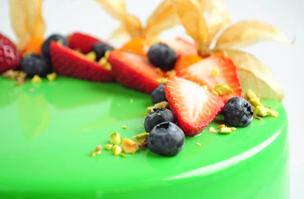 Modern French mousse cake with green mirror glaze and with berries, pistachios.