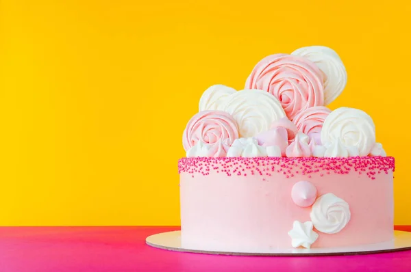 Birthday pink cake for girl, decorated with marshmallow, meringue cookies on a yellow pink background.