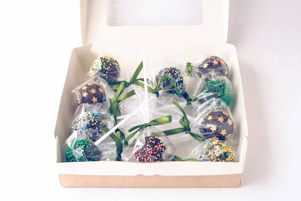 Chocolate cake pops, packed in a transparent film, bandaged with a green ribbon, lie in a box. Toned.