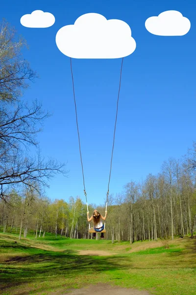 Girl swinging on high swing, suspended to the drawn cloud, against the background of a spring forest and  blue sky.