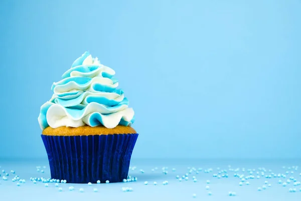 Cupcake on birthday with blue and white cream on blue background, decorated with sprinkles.
