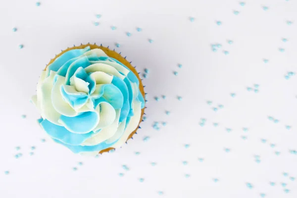 Cupcake on birthday with blue and white cream on white background, decorated with sprinkles. Top view.