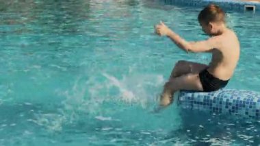 Havuz kenarında oturan ve bacakları su sıçramasına tekme çocuk