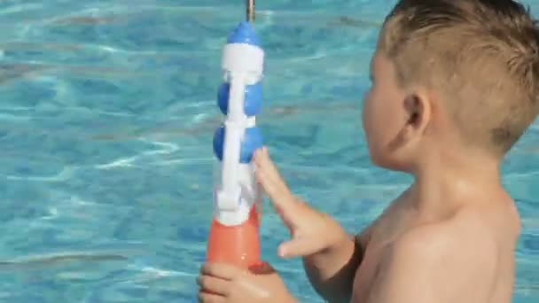 Kleiner Junge spielt mit Wasserpistole im Pool — Stockvideo